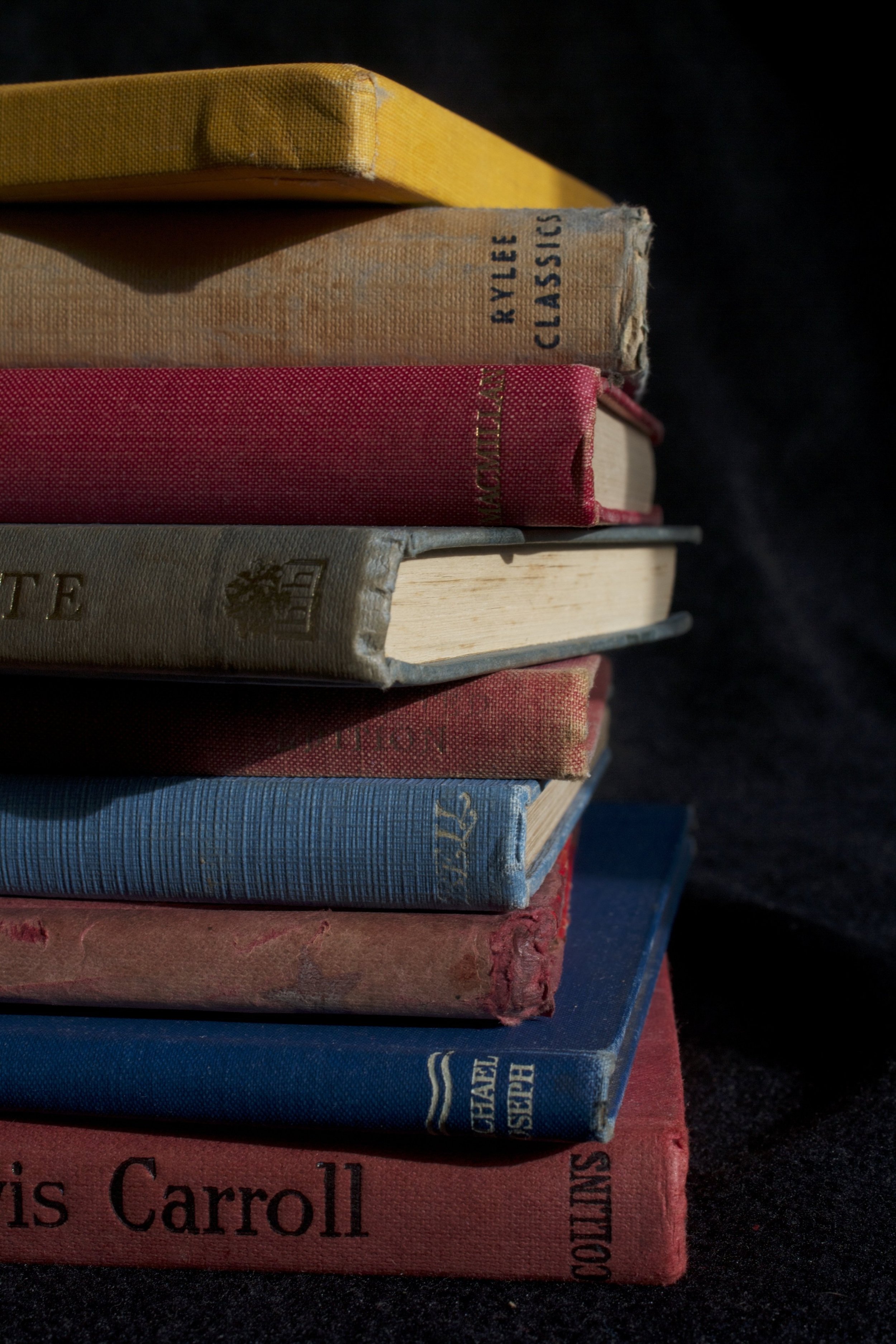 Stack of colorful worn books, including titles like 'Jane Eyre', 'Charlotte', and 'Crossed' on a dark surface.