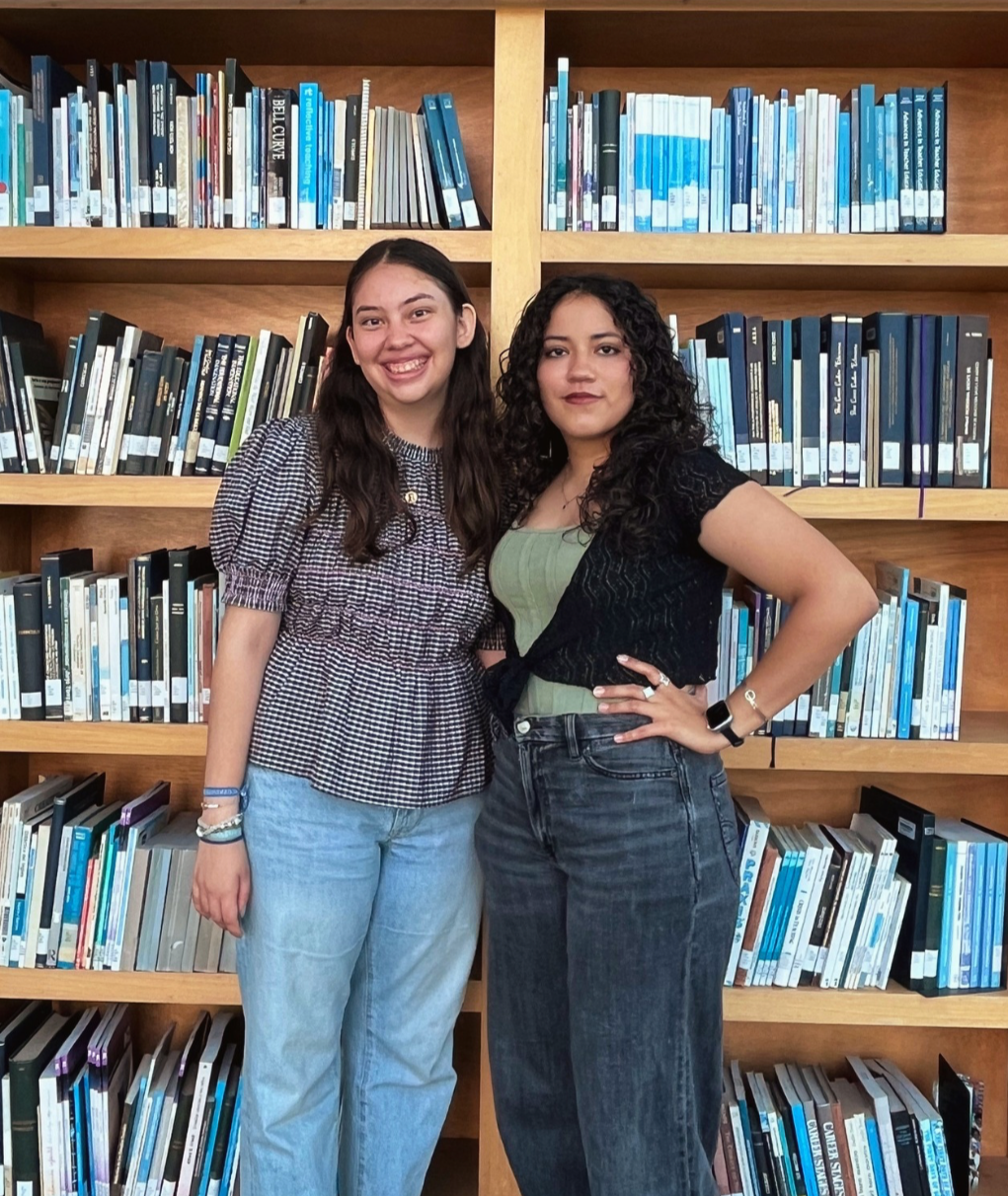 Two young women standing in front of a bookshelf filled with books at a library.