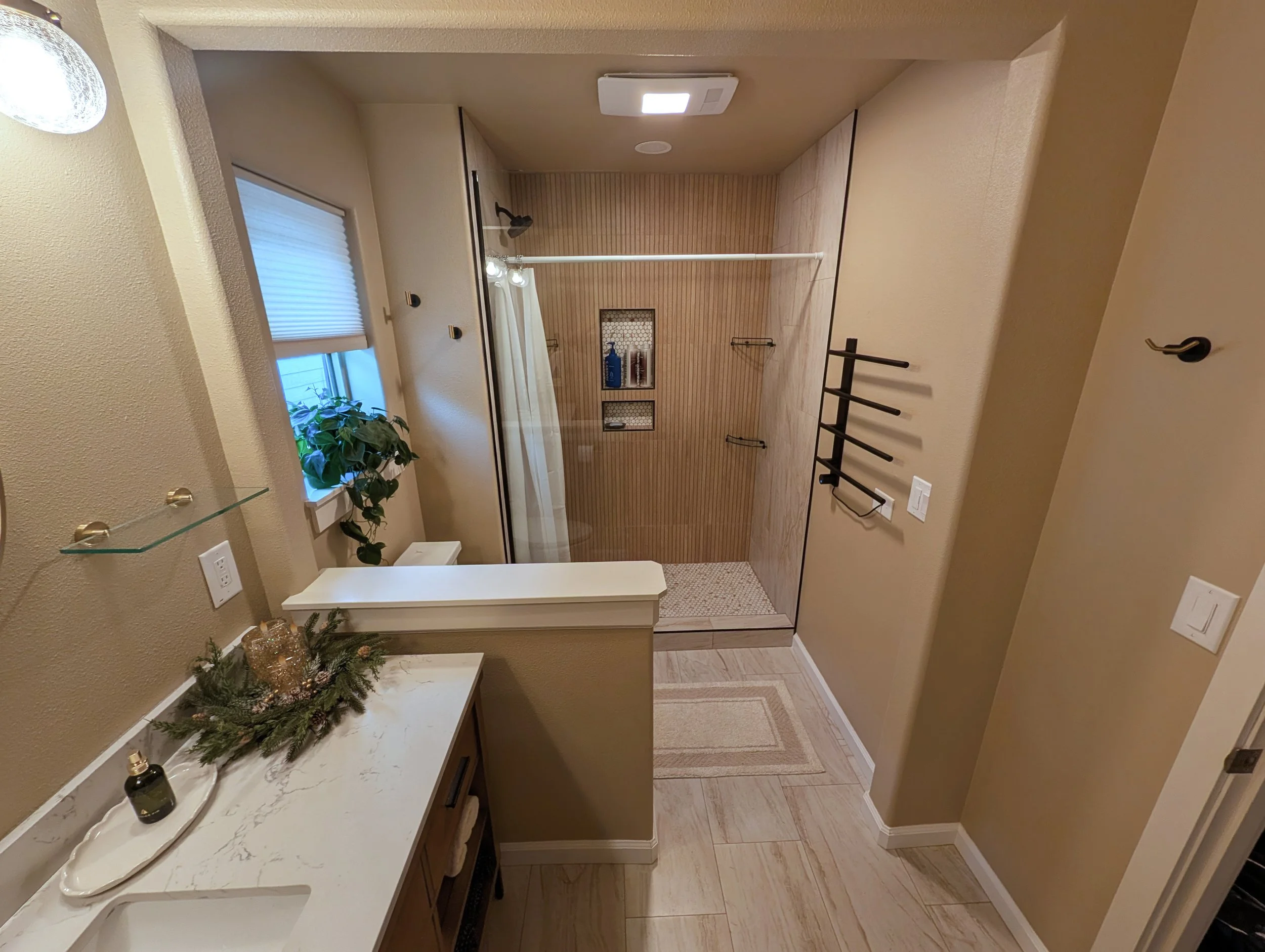 A small bathroom with a vanity, soap, and decorations, seen from the doorway with a view into the shower area with a curtain and white tiled walls.