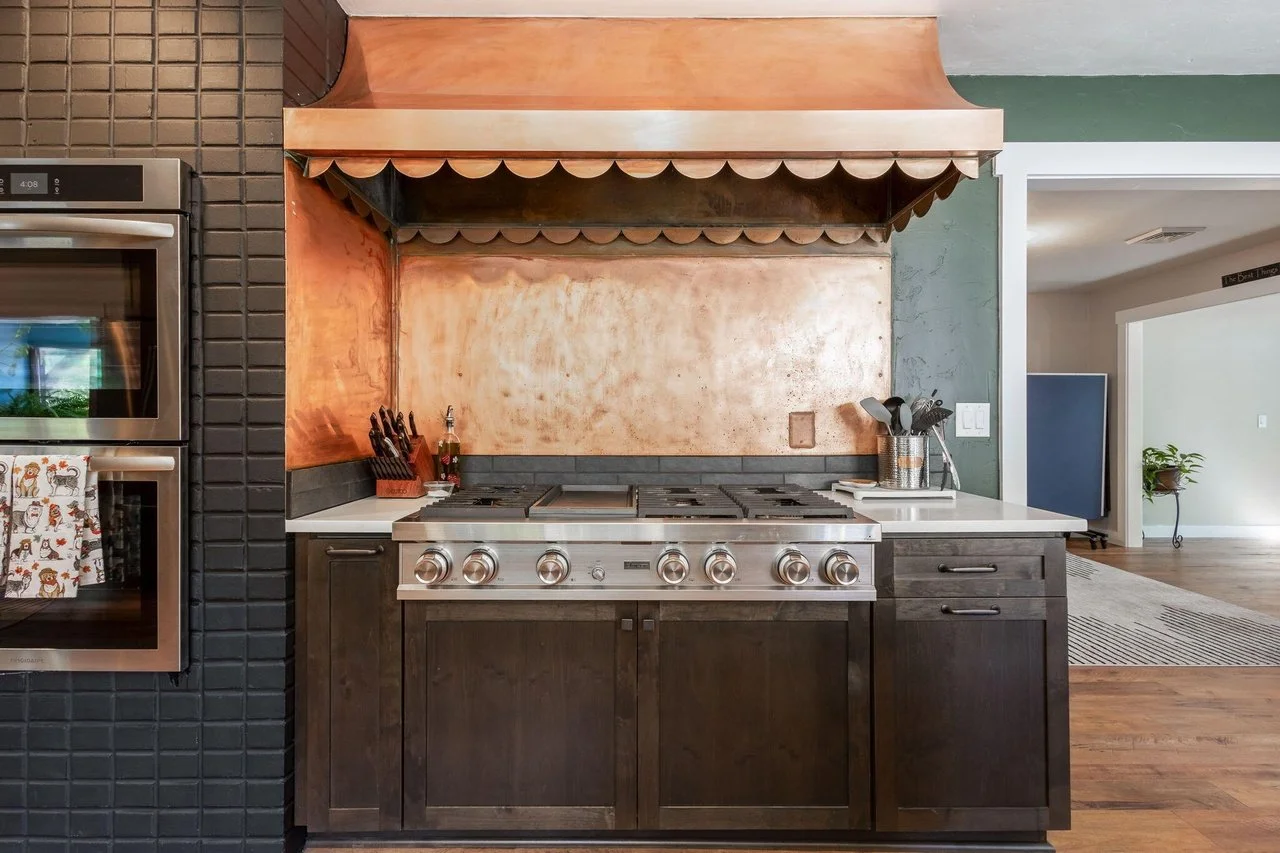 Kitchen with a stainless steel oven, dark wood cabinets, a stainless cooktop, copper backsplash, and a copper range hood.