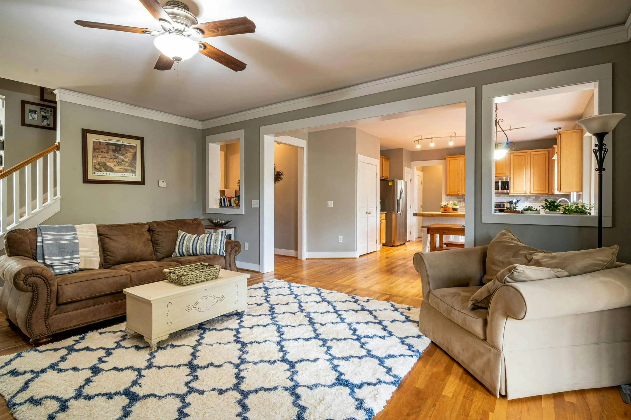 Open concept living room with a brown sofa, beige armchair, white coffee table, and a blue and white patterned rug.