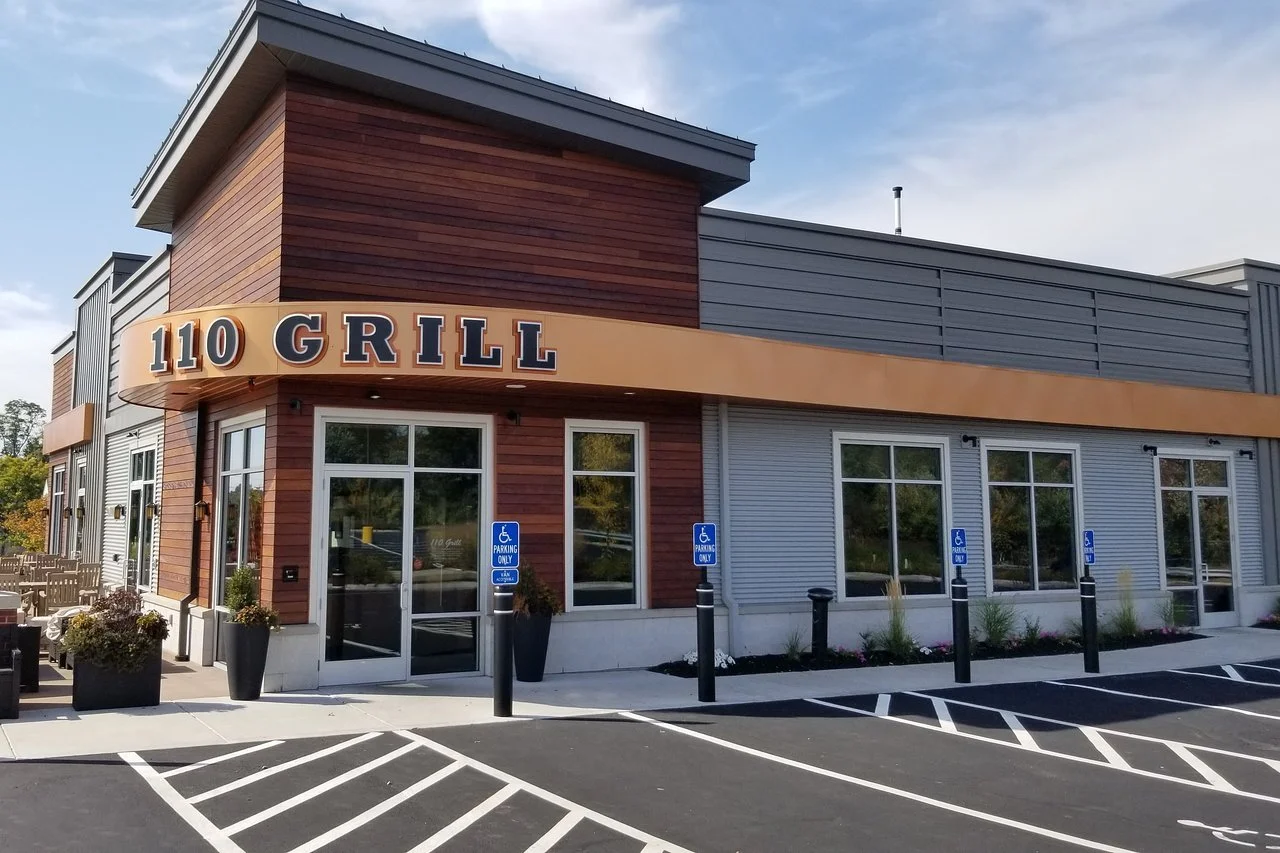 Exterior view of a modern building with a sign that reads "110 Grill" and a parking lot with designated handicapped parking spaces.