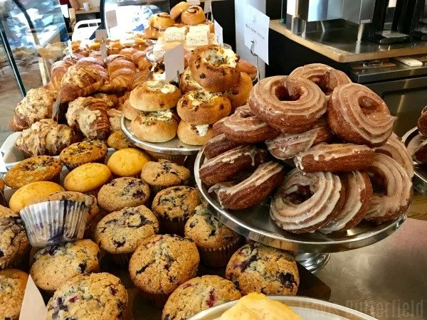 Assorted baked goods, including croissants, cookies, muffins, and donuts on display in a bakery.