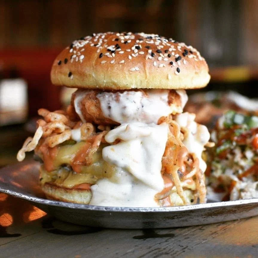 A fried chicken sandwich with a sesame seed bun, topped with mayonnaise and shredded chicken, served with a side of coleslaw.