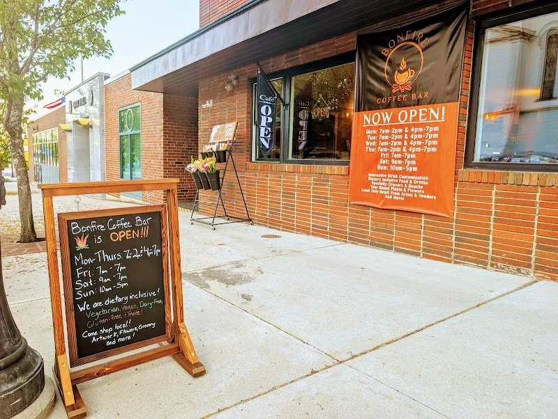 Corner of a brick coffee shop with an outdoor chalkboard sign and a large orange banner reading "Now Open".