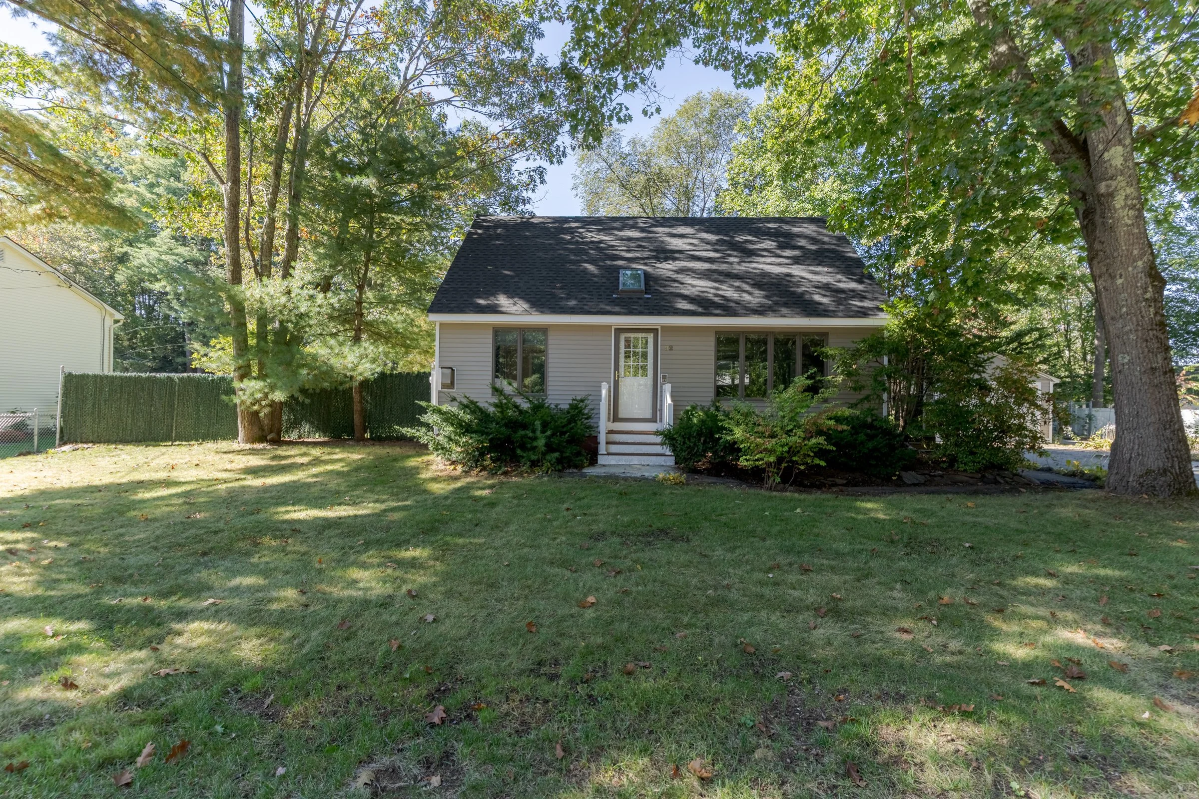 A small house with a front porch, surrounded by trees and daytime sunlight filtering through the leaves.