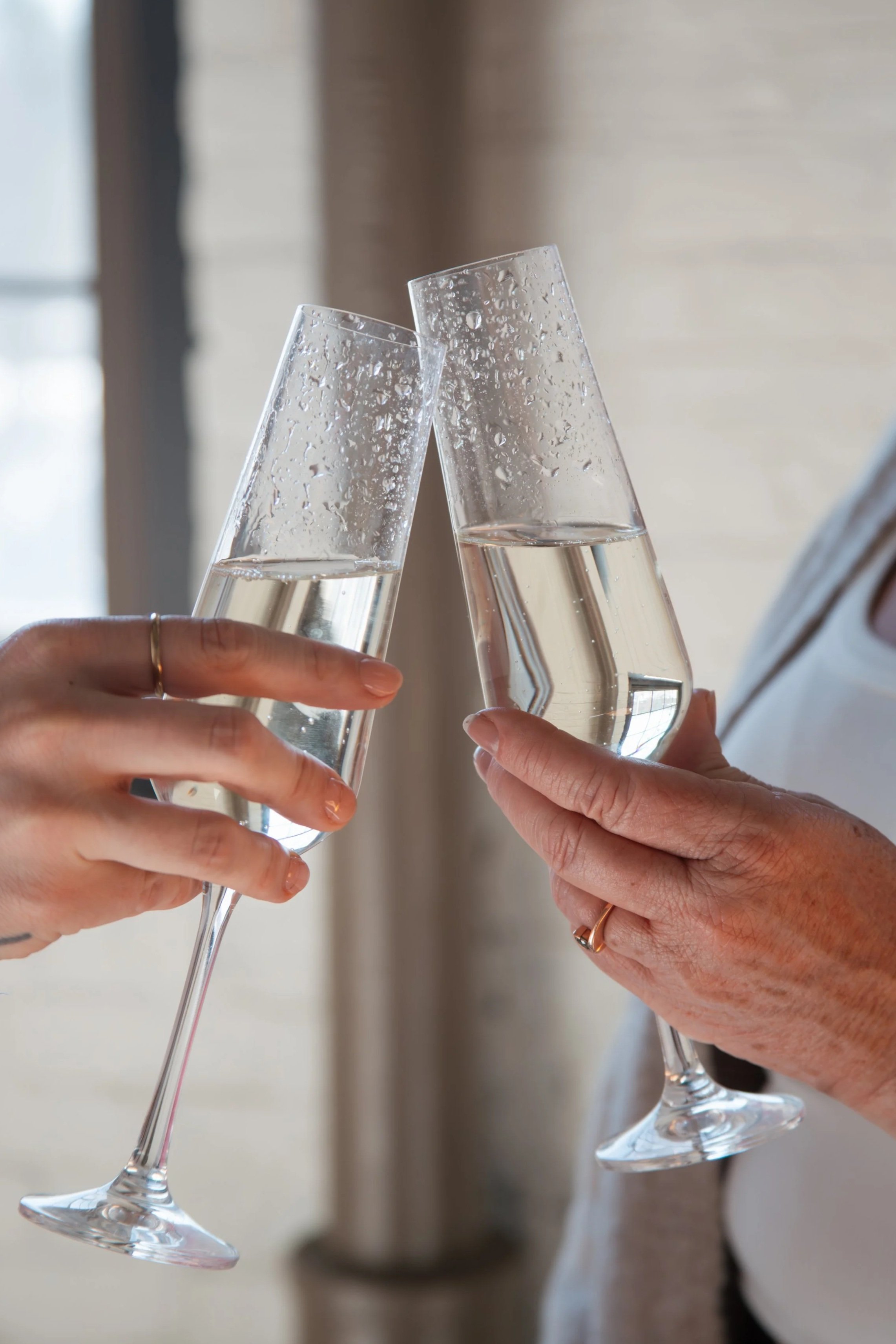 Two hands holding champagne flutes filled with sparkling wine, clinking together in celebration.