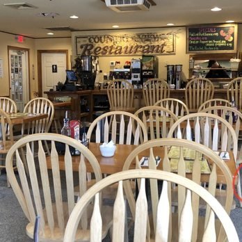 Interior of a restaurant with empty wooden chairs and tables, a counter with coffee machines, and a chalkboard menu on the wall.