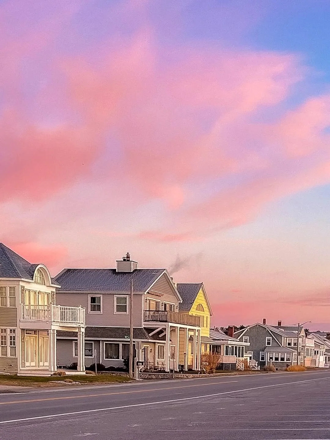 A row of colorful houses along a street during sunset with pink and purple clouds in the sky.