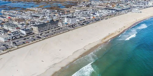 Aerial view of a sandy beach along the ocean with city buildings in the background.