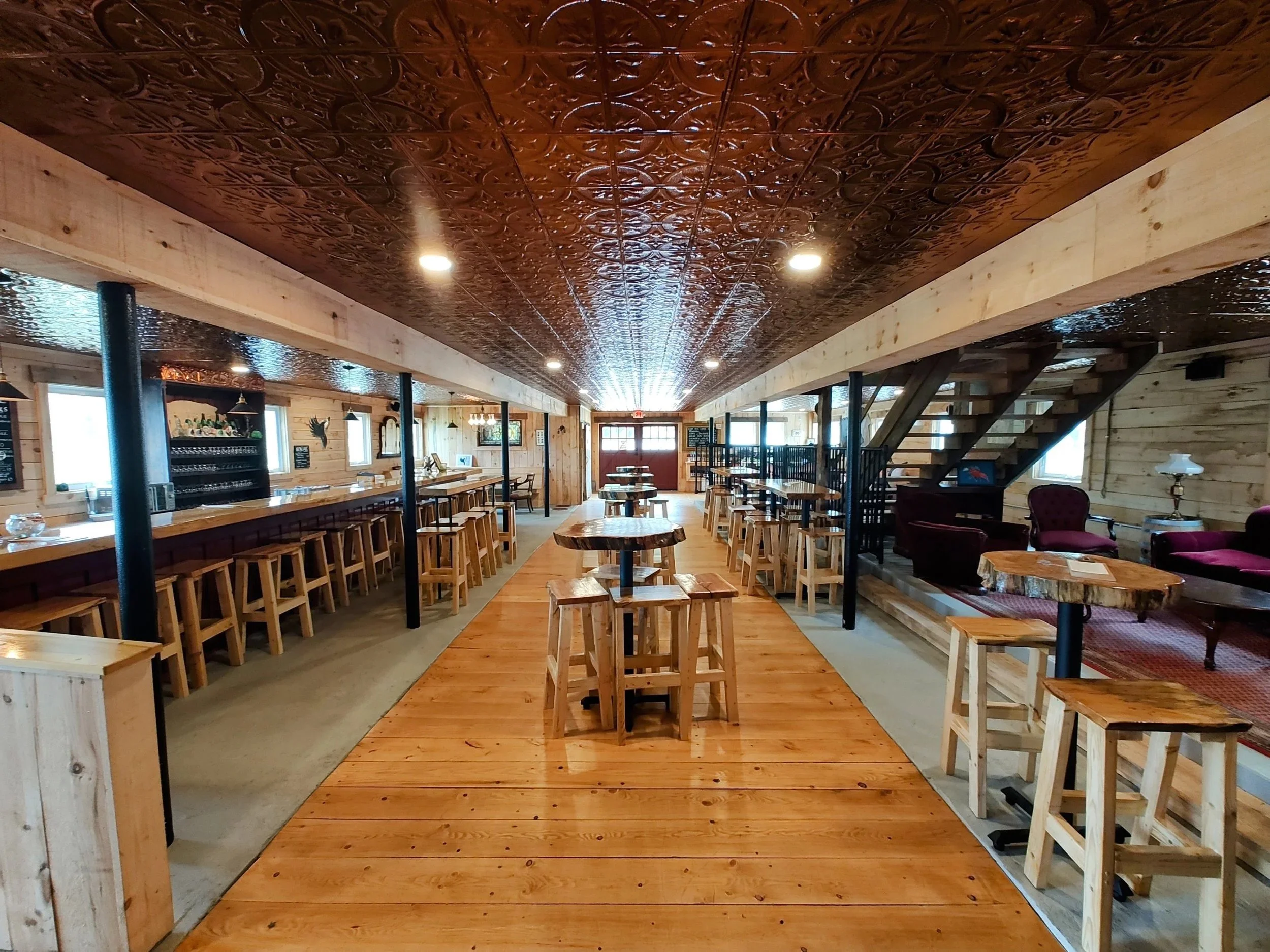 Interior of a cozy wooden restaurant or cafe with a long bar counter, wooden tables and benches, decorative ceiling, and warm lighting.