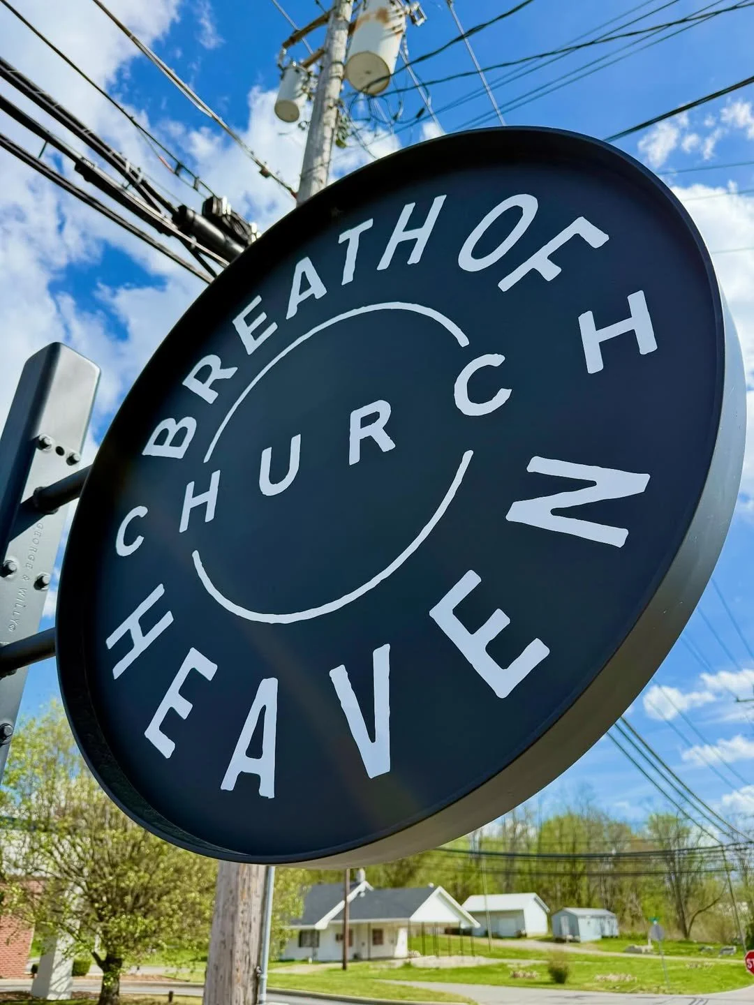 Sign for Breathof Church Hill Avenue, with overhead power lines, blue sky with clouds, and small houses and trees in the background.
