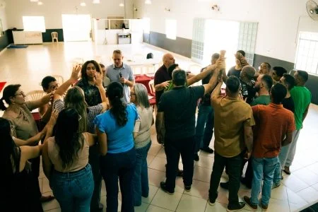 A group of people gathered in a room, participating in a group activity or discussion, with some raising their hands.