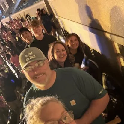 Group of young people and an older man standing in line outside at night, with other people in the background.