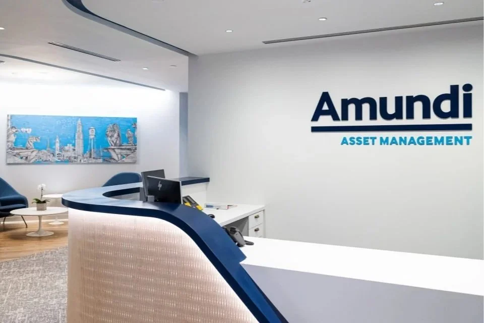 Reception area of Amundi Asset Management office with a curved reception desk, a computer, seating area with chairs and a painting of a city skyline on the wall.