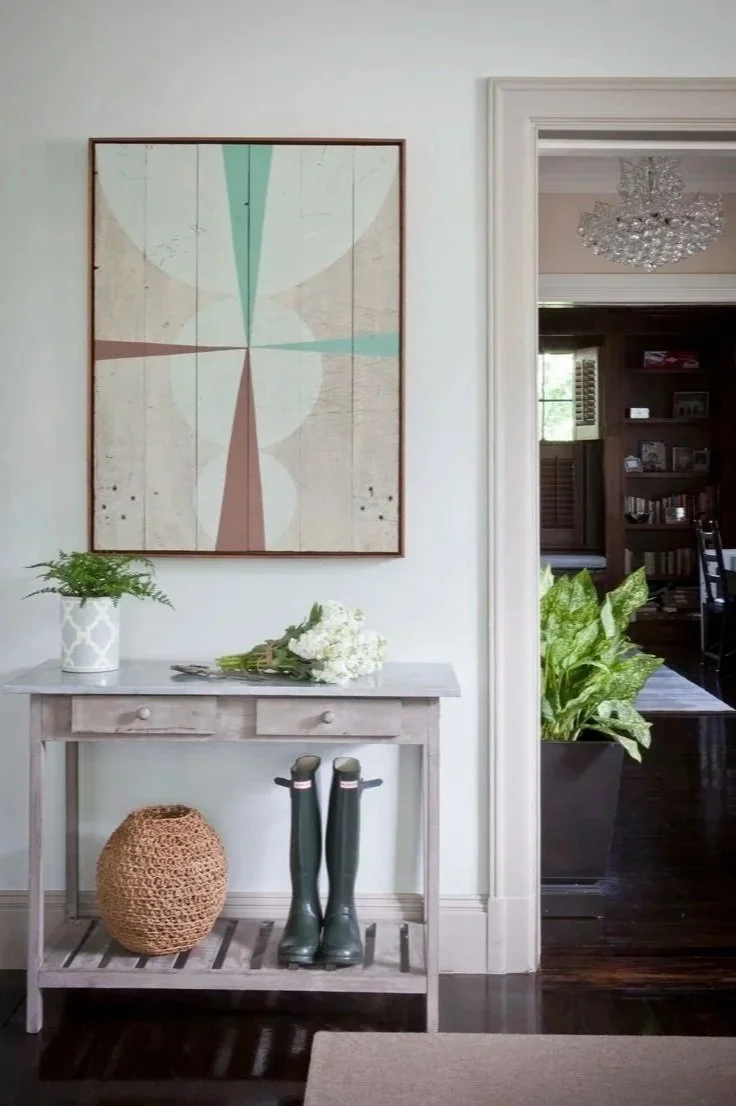 Entryway with abstract artwork, white console table, flower bouquet, green plants, and green rain boots.