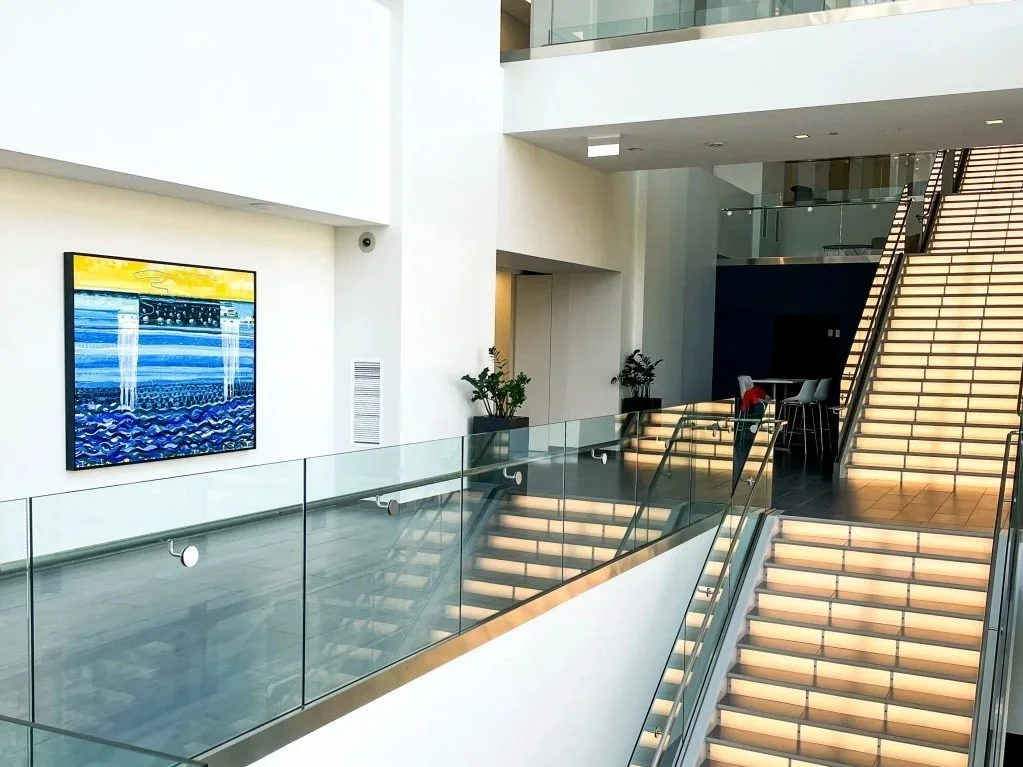Modern indoor space with staircase, glass railings, minimal decor, and artwork on the wall.