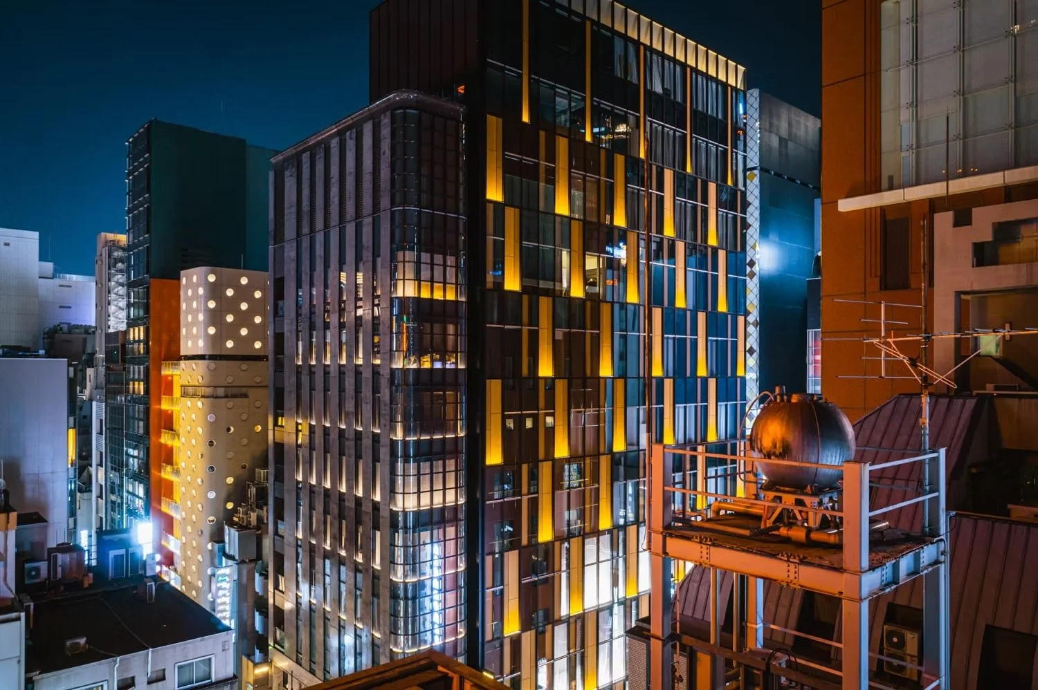 Nighttime cityscape with illuminated modern high-rise buildings and rooftop equipment.