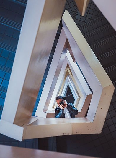A creative self-portrait taken from the center of a geometric staircase, with multiple triangular frames leading the viewer’s eye towards the photographer.