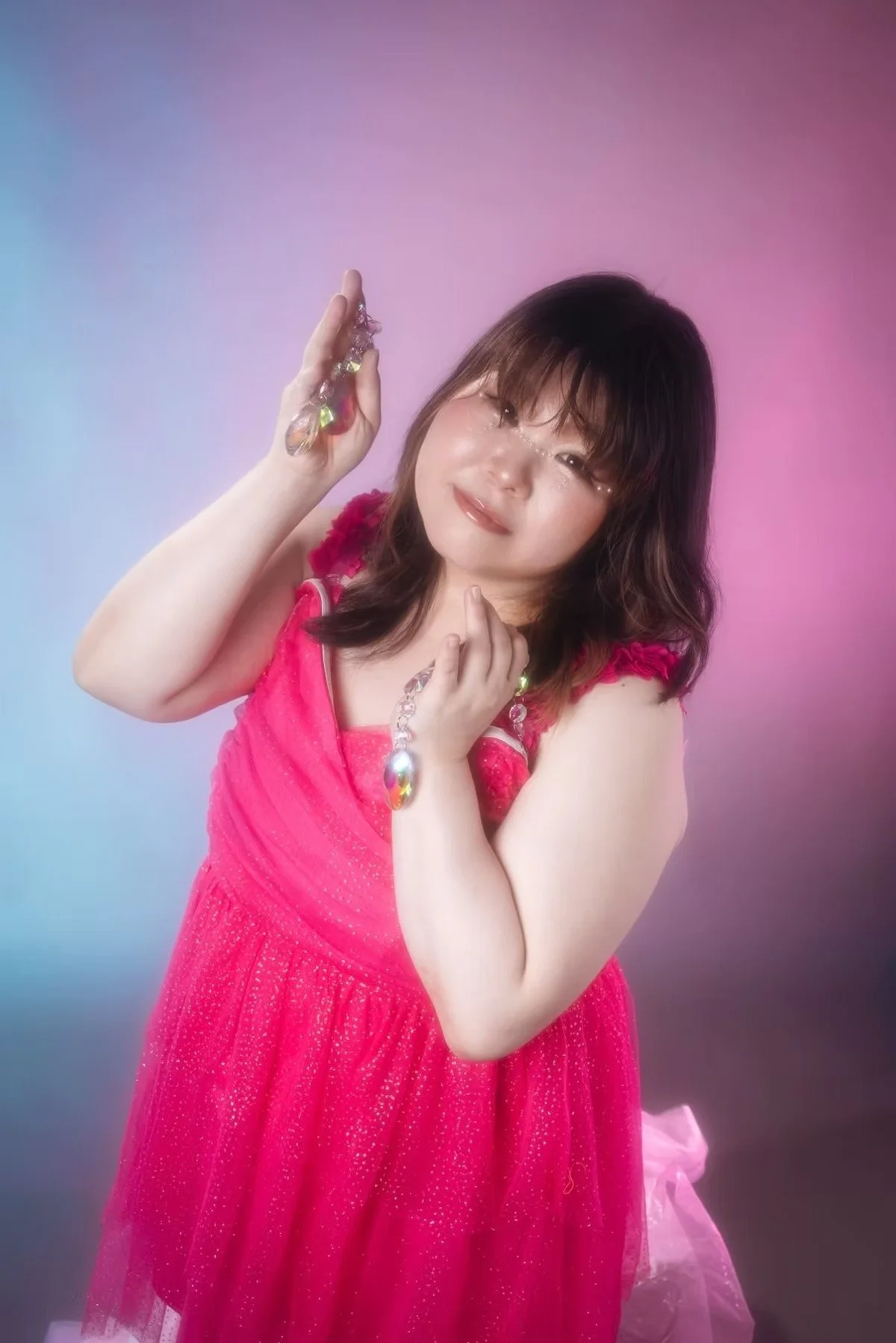 A woman in a flowing pink dress strikes a playful pose, creating a soft and dreamy atmosphere. The vivid pink backdrop and delicate lighting enhance the romantic charm.