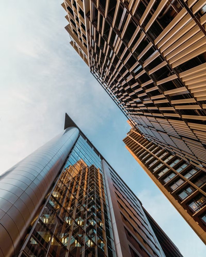 Looking up at tall modern skyscrapers with glass and metal exteriors against a clear sky. Deniz Demir photography