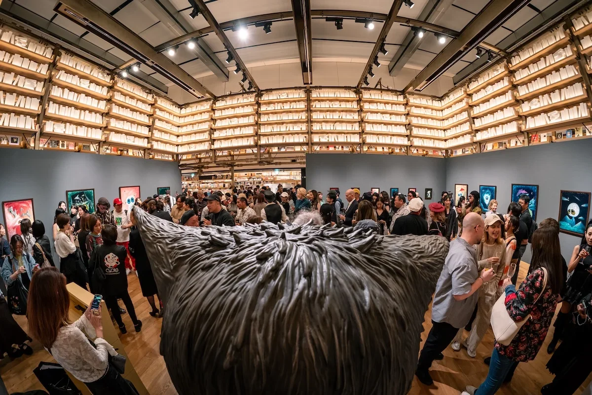 August Vilella
---
Guests pose together in front of August Vilella's distinctive surrealist paintings, featuring fantastical creatures with oversized golden eyes, during a contemporary art exhibition and gallery event.