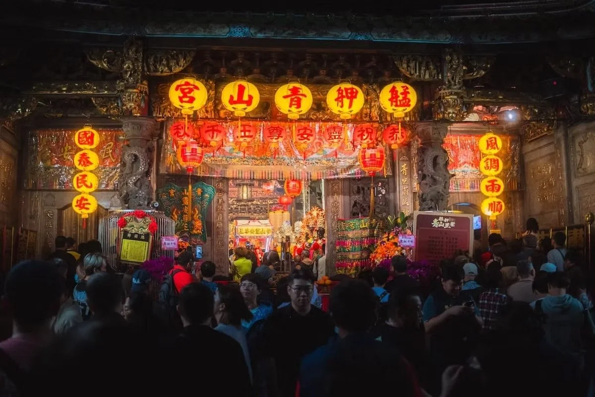 Crowd inside a traditional temple decorated with lanterns, banners, and intricate wood carvings, celebrating a festival or religious event. Taiwan traditional temple in Taipei.