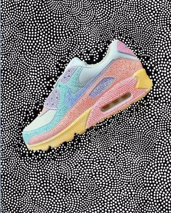A close-up shot of a multicolored Nike sneaker with a dotted, abstract background. The sneaker features pastel hues of blue, pink, yellow, and green.