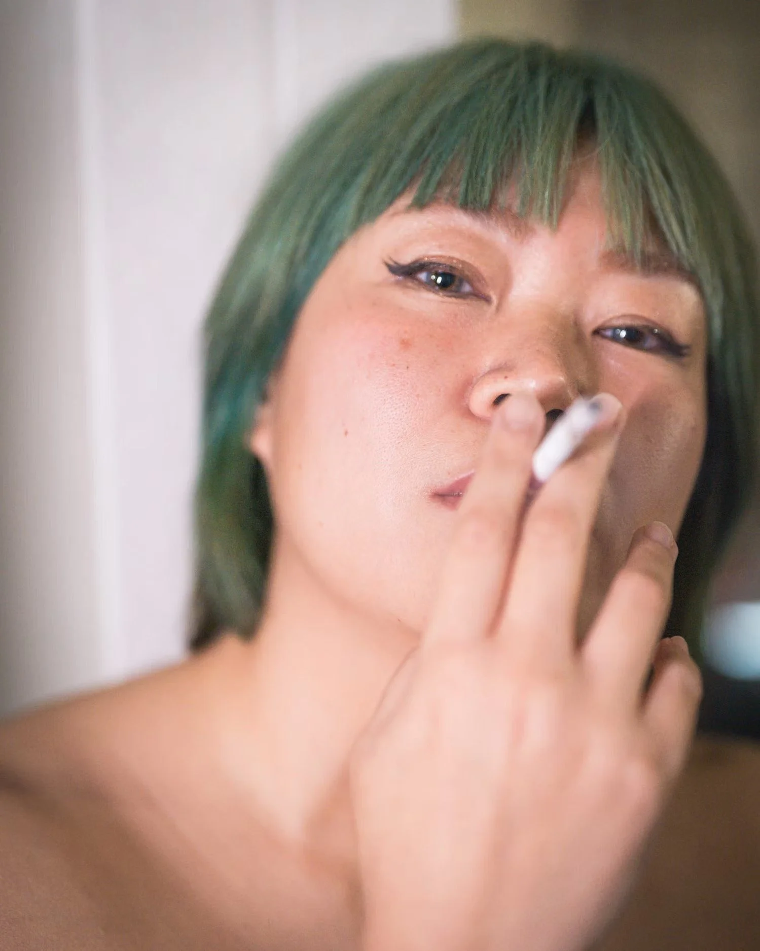 Close-up of a woman with green hair applying makeup or grooming her face.