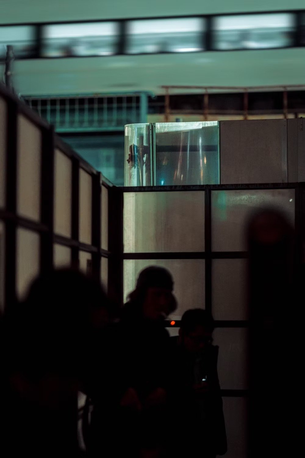 Dark indoor scene with silhouetted people in the foreground and colorful, reflective architectural elements in the background. Nakano at night.