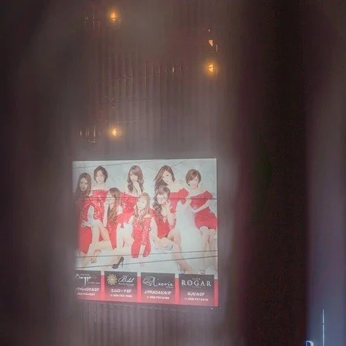 A foggy window view of a red-themed poster featuring a group of women in glamorous outfits, illuminated by warm interior lights.