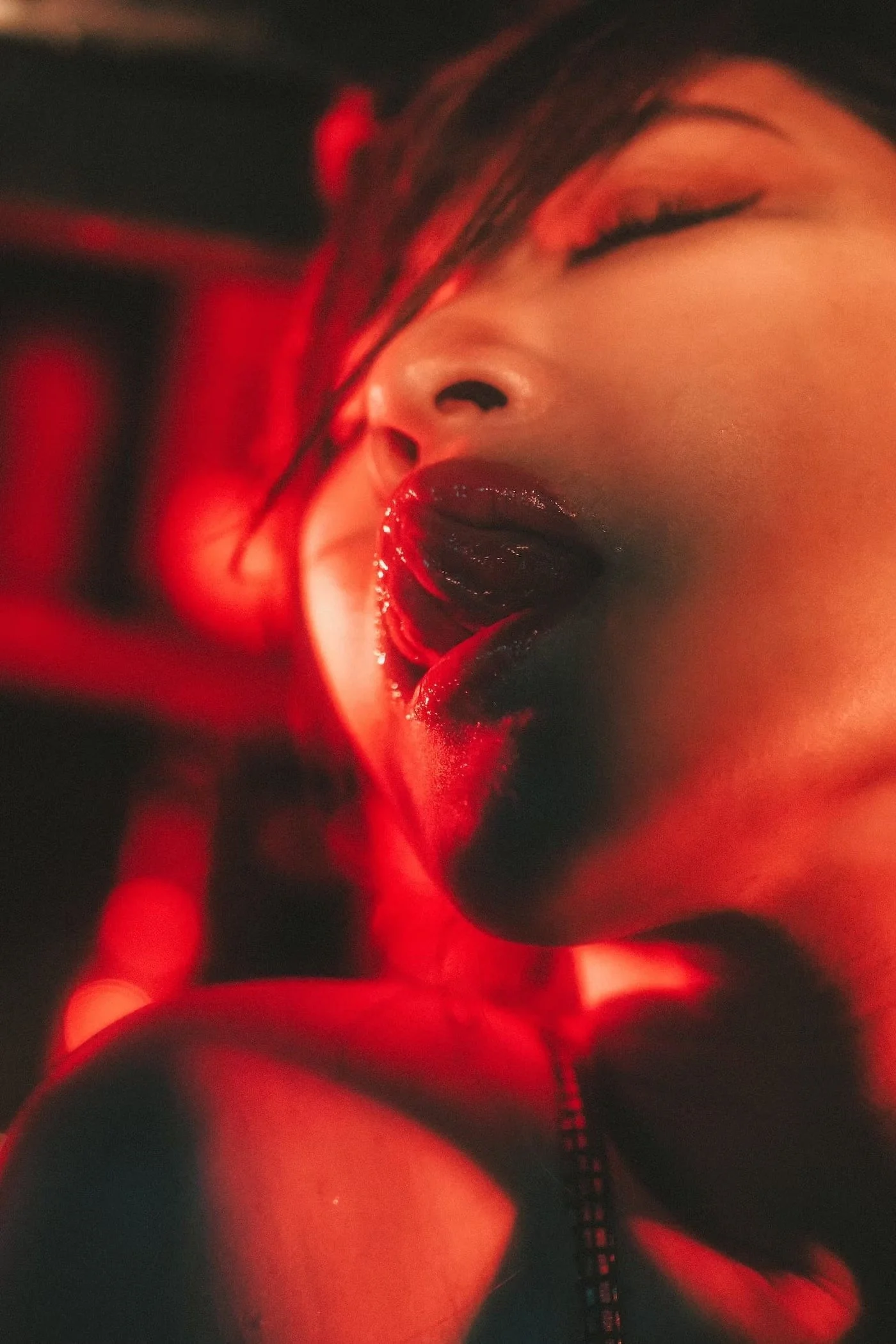 Close-up of a woman with dark hair, bold makeup, and red lipstick, in a sensual pose with red lighting.
