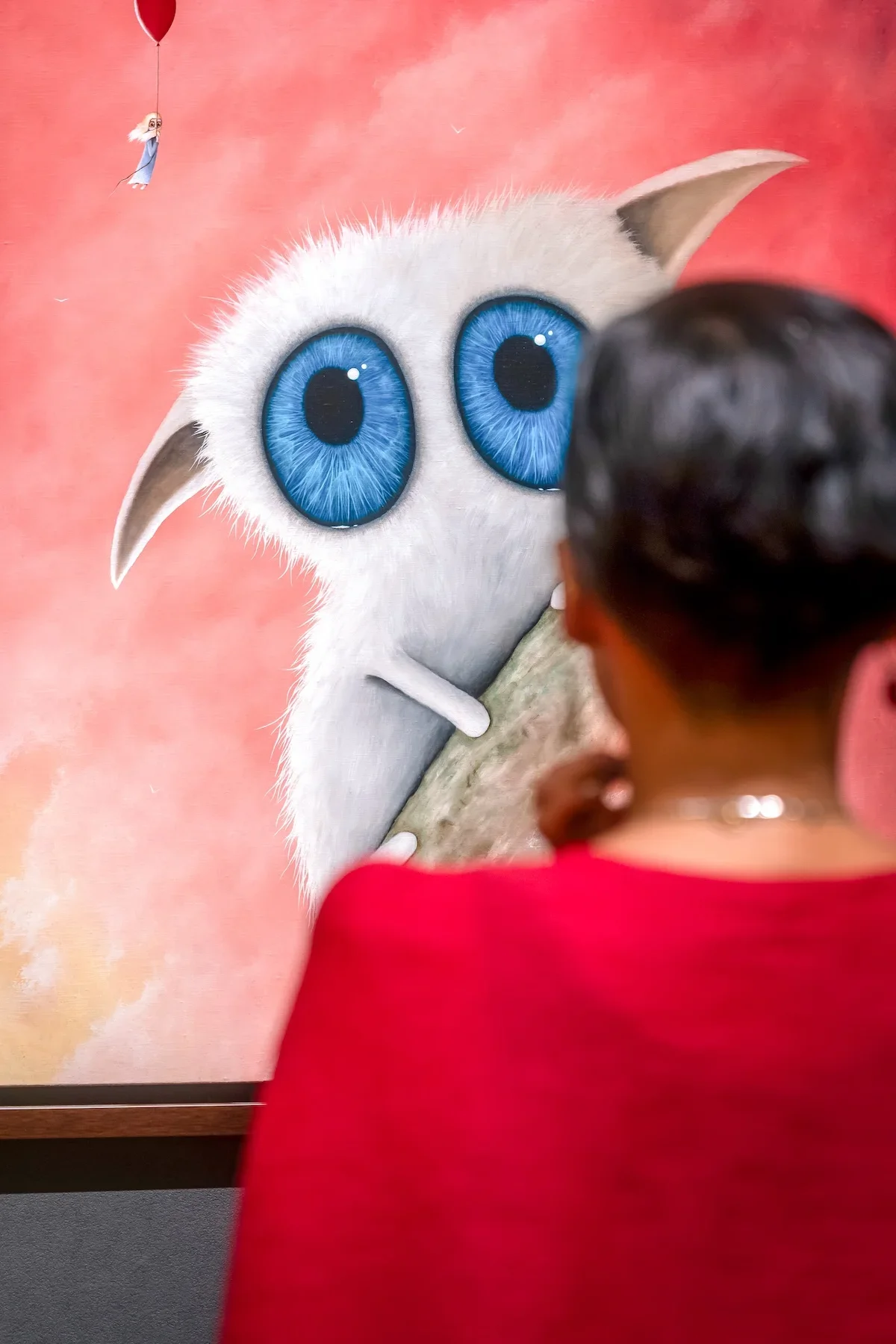 August Vilella
---
A visitor in a red top admires a surrealist painting featuring a white, wide-eyed creature against a vibrant pink background at an art exhibition showcasing the imaginative work of contemporary artist August Vilella in Ginza, Tokyo