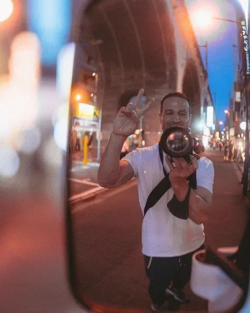 A photographer capturing a moment in a mirror, with the vibrant lights of Tokyo in the background. A perfect shot taken during the Tekumi Photowalks workshop street photography.
