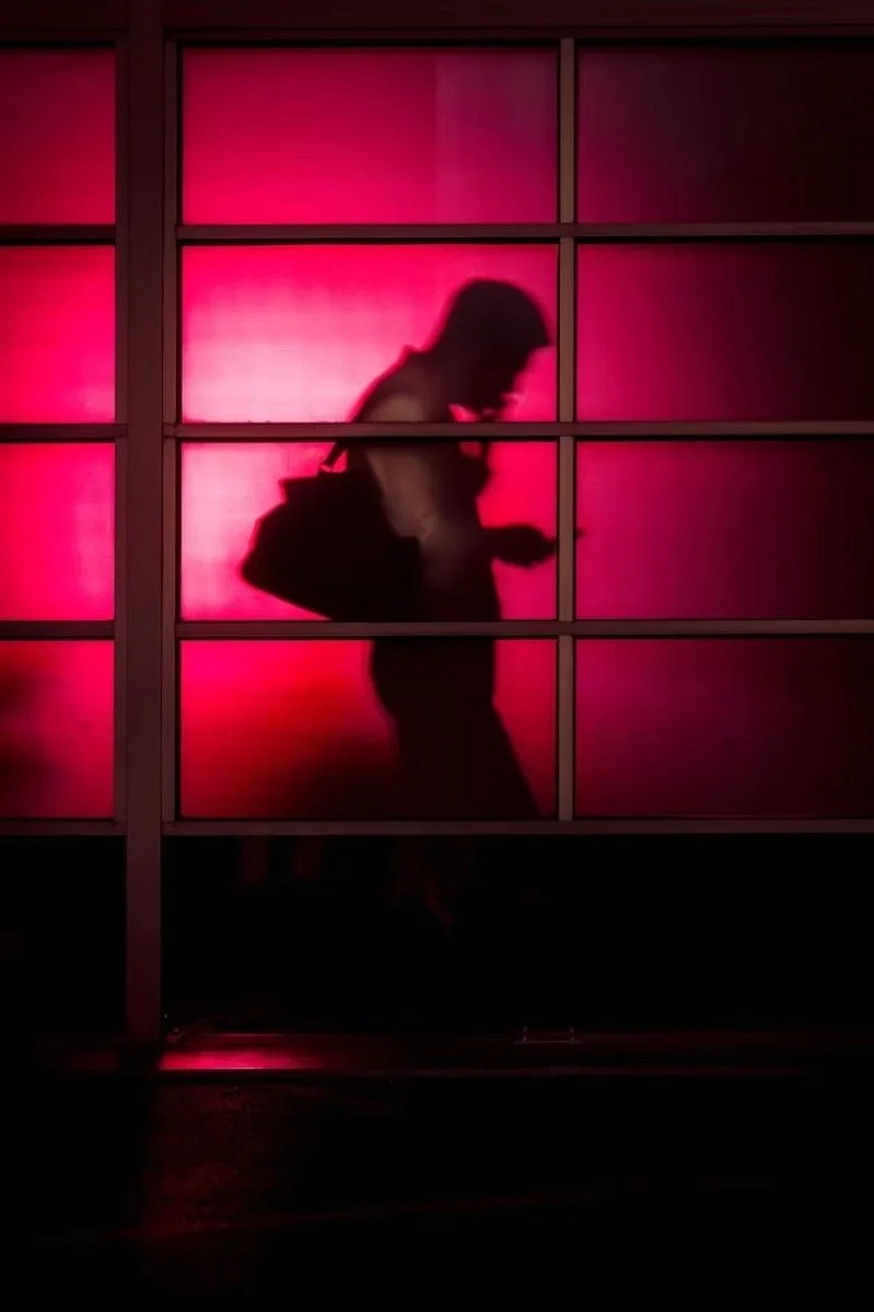 Silhouette of a person with a backpack walking, seen through a window with pink lighting in the heart of Shimbashi Tokyo.