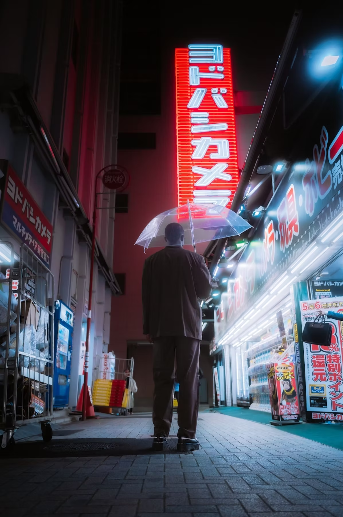 A man wearing a suit holds an umbrella while walking down a neon-lit street in Tokyo at night. Vibrant signs illuminate the scene.