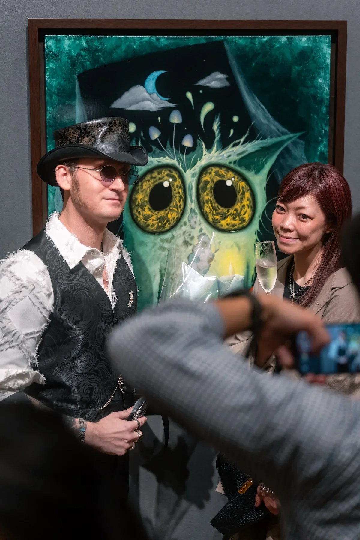 August Vilella
---
Guests pose together in front of August Vilella's distinctive surrealist paintings, featuring fantastical creatures with oversized golden eyes, during a contemporary art exhibition and gallery event.