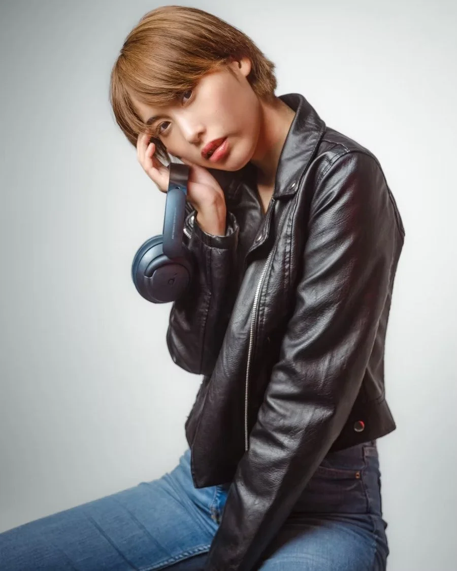 A woman dressed in a black leather jacket strikes a contemplative pose, highlighted by warm tones that emphasize her effortless cool style.