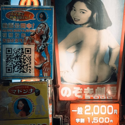 A poster of a woman with black hair posing topless, with Japanese text and a price listed as 2,000 yen, and hinting at lower price options.