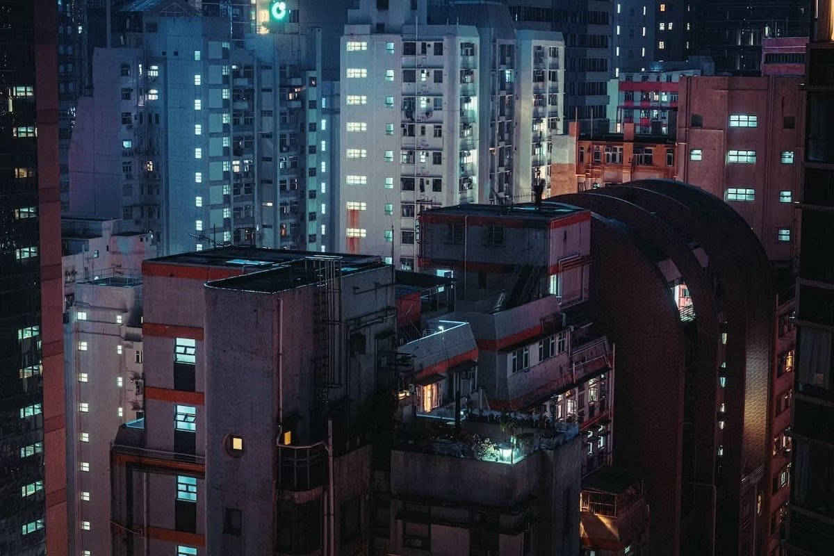 Nighttime cityscape of high-rise buildings with illuminated windows and rooftop lights.