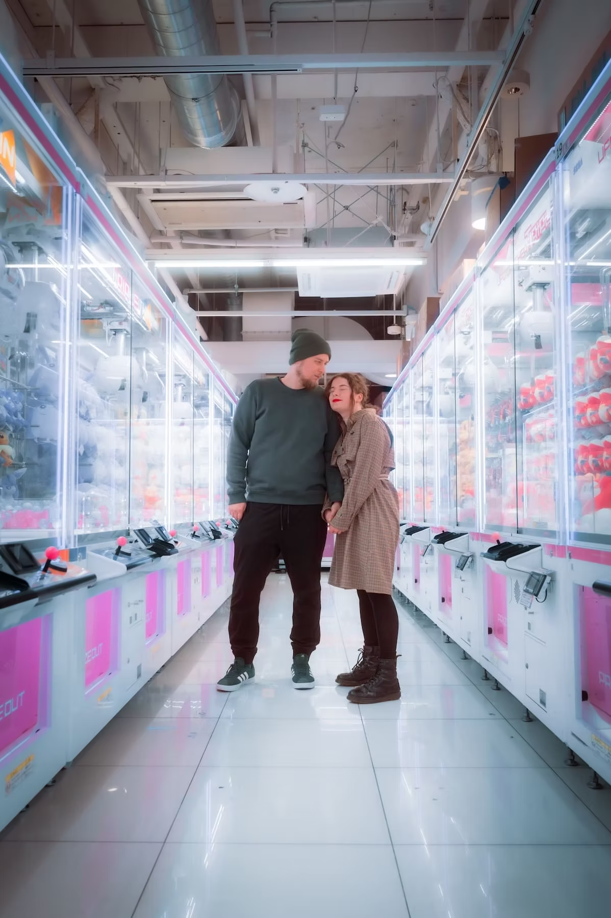 A couple stands close together in a bright vending machine arcade in Tokyo, surrounded by rows of machines that glow with pink and white lights.