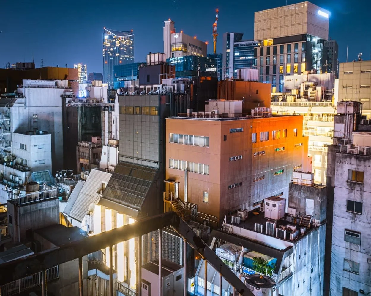 Nighttime cityscape of densely packed buildings with colorful lights and high-rise structures in the background.