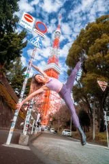 A person in a purple outfit performing a handstand on a street, with a tall red and white tower and trees in the background.