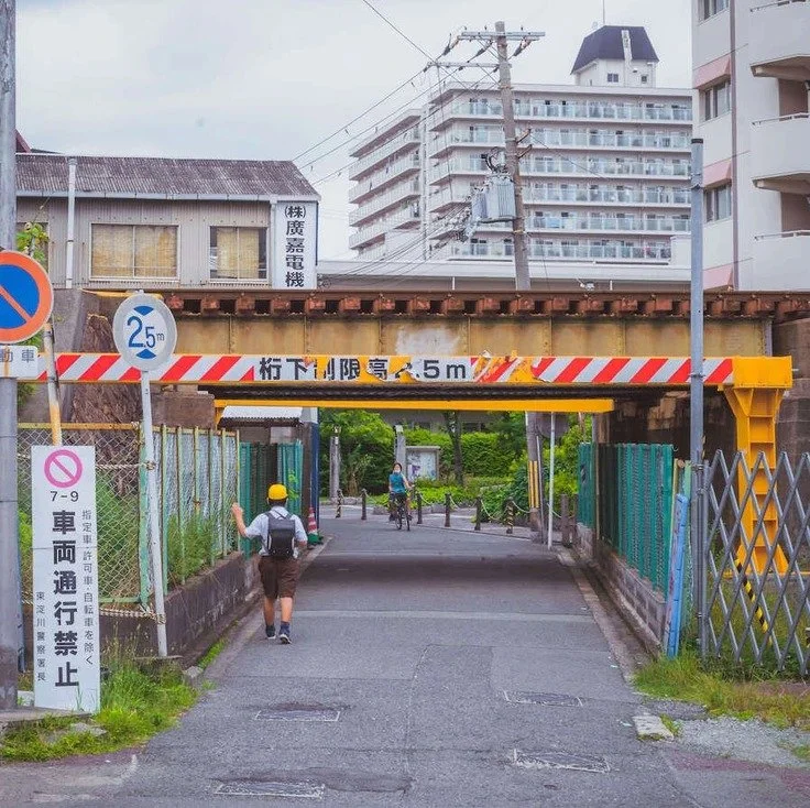 A person walking under an overpass with a sign indicating height clearance in Osaka, captured during street photography.