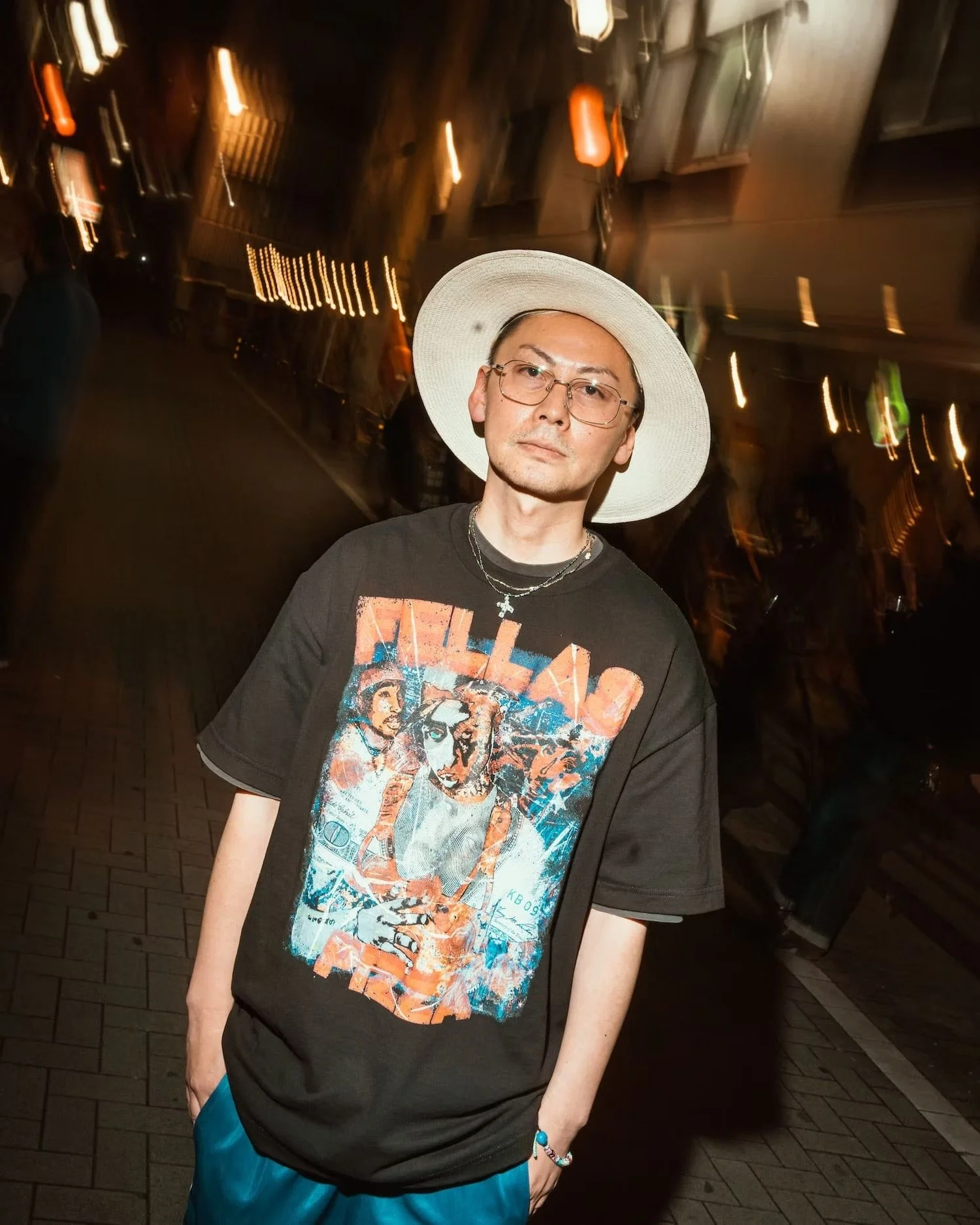 Man posing in Shibuya at night wearing graphic t-shirt and sunglasses.