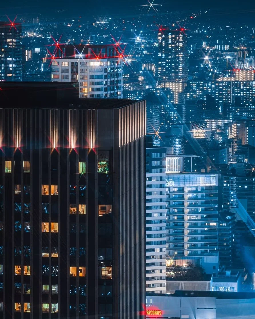 Night view of a illuminated cityscape with high-rise buildings and bright lights, creating a starburst effect.