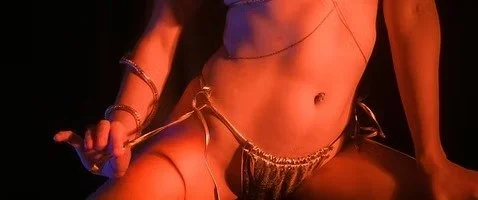 Close-up of a woman's midsection and legs, wearing gold accessories and metallic clothing, against a dark background.