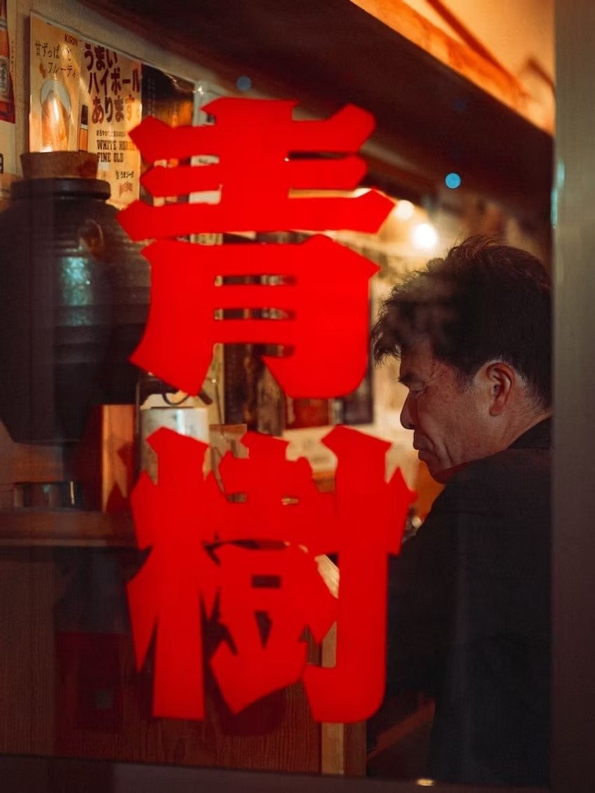 Red paper lanterns and Japanese characters hanging in a restaurant, with a man sitting inside, partially visible in profile.