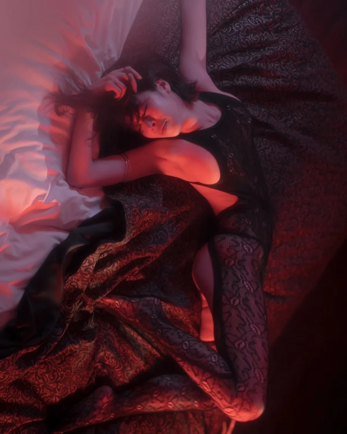 A woman in black lingerie lying on a red velvet blanket, with moody red lighting. Boudoir Photography by Tokyo Photographer Deniz Demir. Japan.