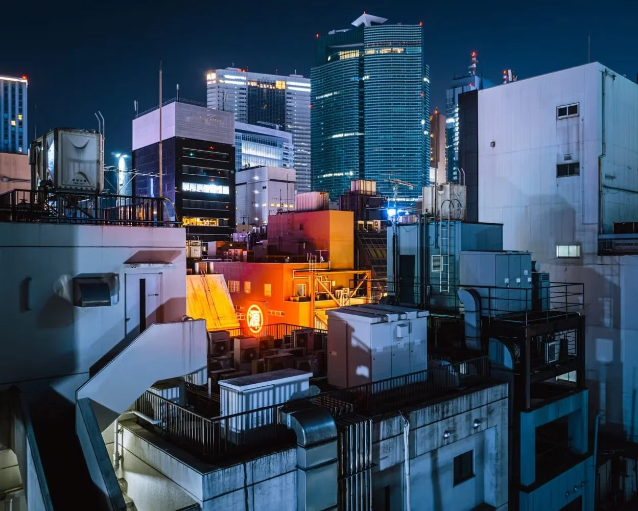 Night Tokyo cityscape with rooftop view of buildings, rooftop HVAC units, and illuminated skyscrapers in the background.